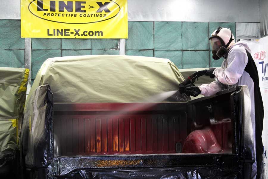 Man wearing biohazard suit spraying truck bed with liner